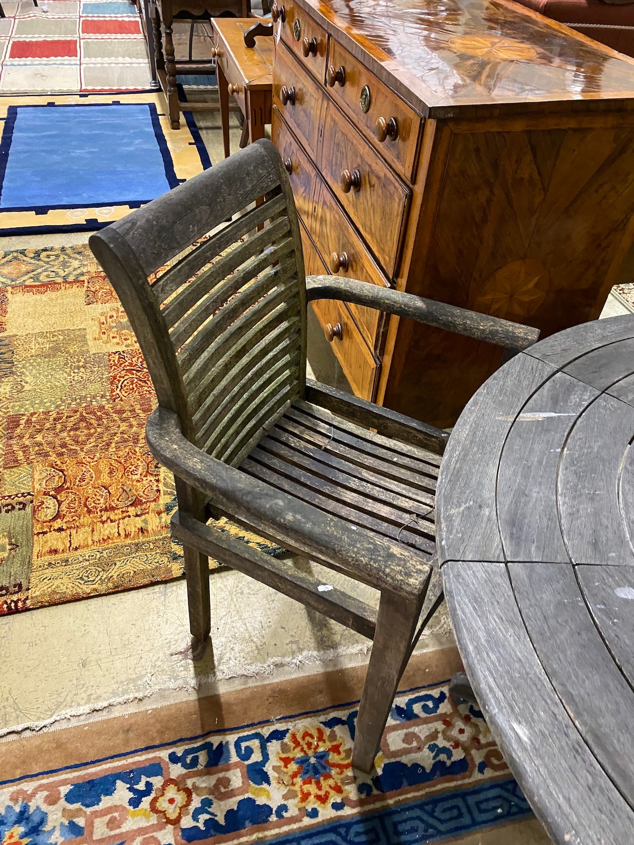 A circular weathered teak garden table, diameter 130cm, height 71cm together with four elbow chairs and a crank parasol